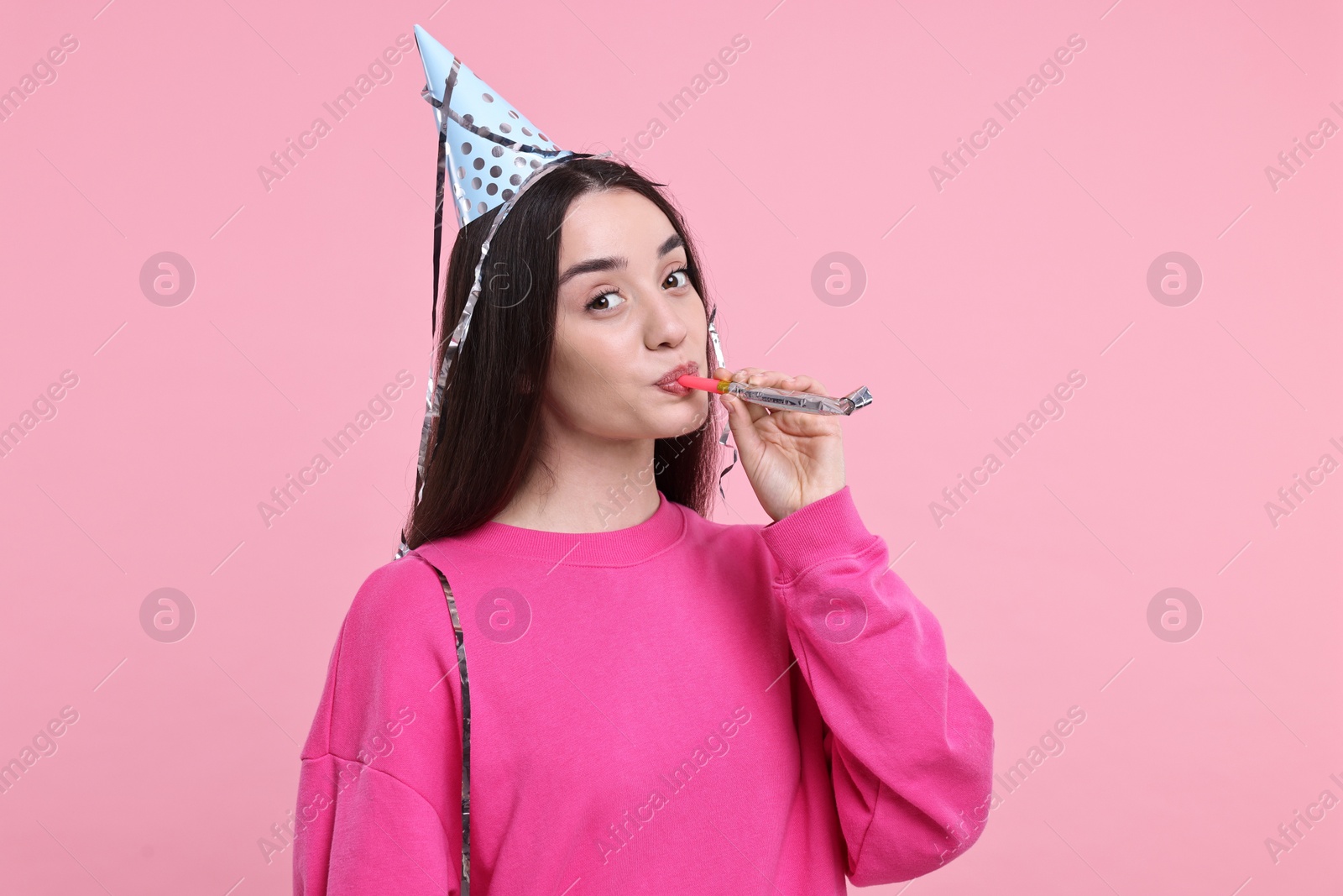 Photo of Woman in party hat with blower and streamers on pink background