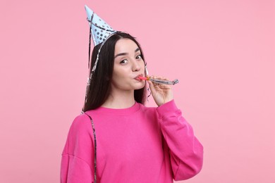 Photo of Woman in party hat with blower and streamers on pink background