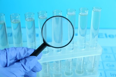 Photo of Scientist with magnifying glass examining test tubes in laboratory, closeup. Color tone effect