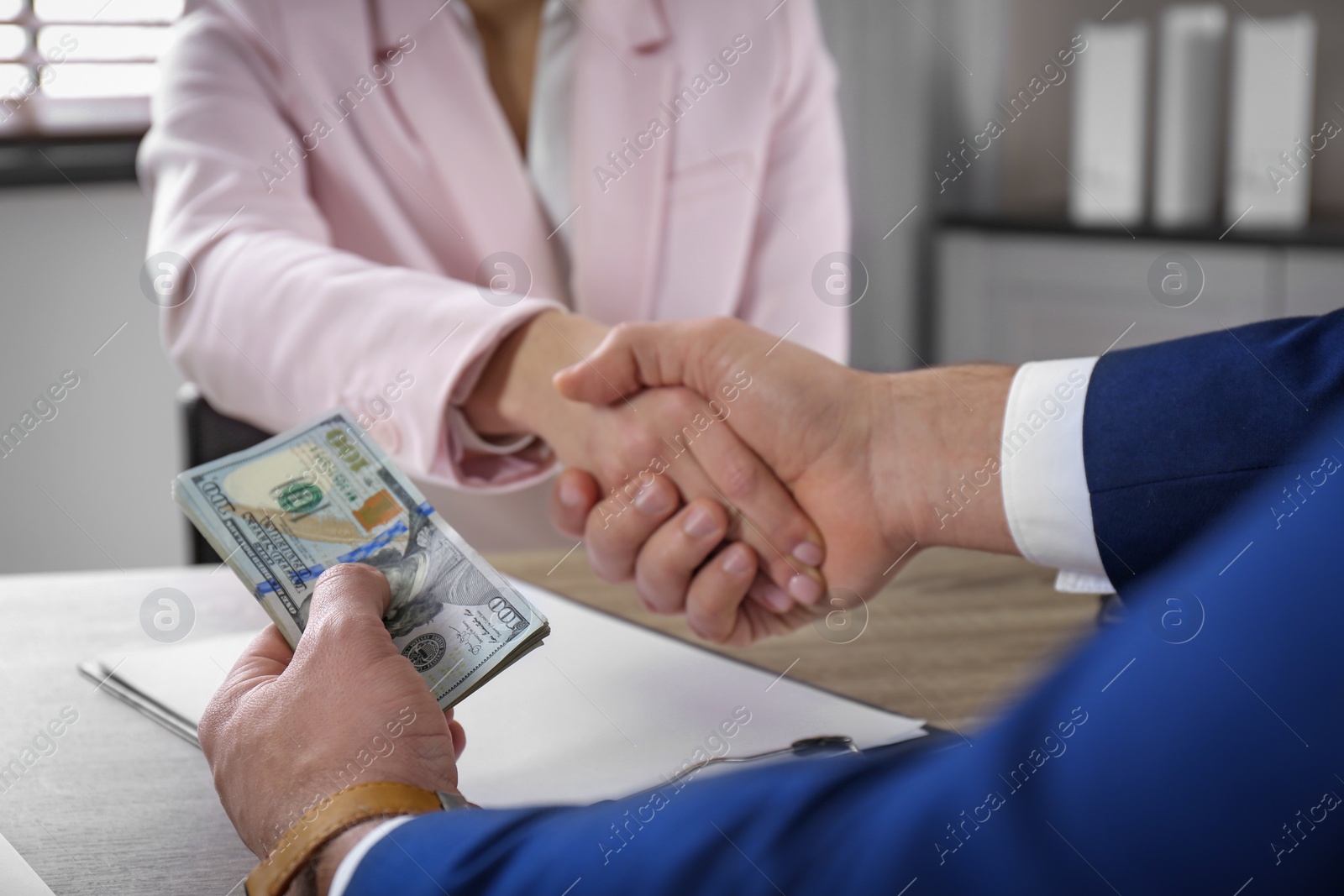 Photo of Man shaking hands with woman and offering bribe at table, closeup