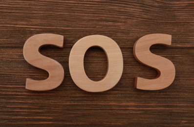 Photo of Abbreviation SOS made of letters on wooden table, top view