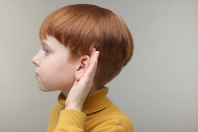 Little boy with hearing problem on grey background, space for text