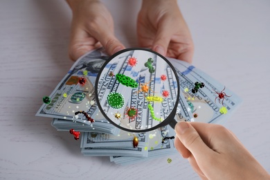 Woman with magnifying glass detecting microbes on dollar banknotes, closeup