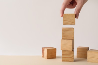 Photo of Woman stacking wooden cubes at table, closeup and space for text. Management concept