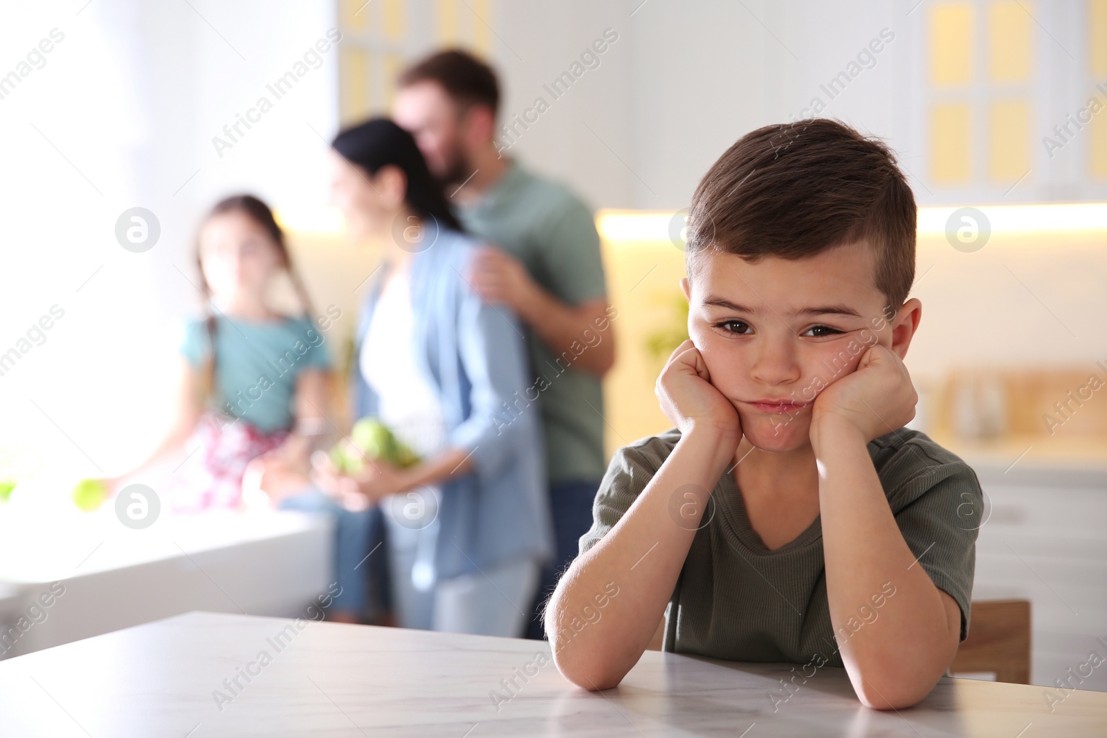 Photo of Unhappy little boy feeling jealous while parents spending time with his sister at home