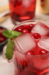 Photo of Tasty cranberry cocktail with ice cubes and mint in glass on table, closeup