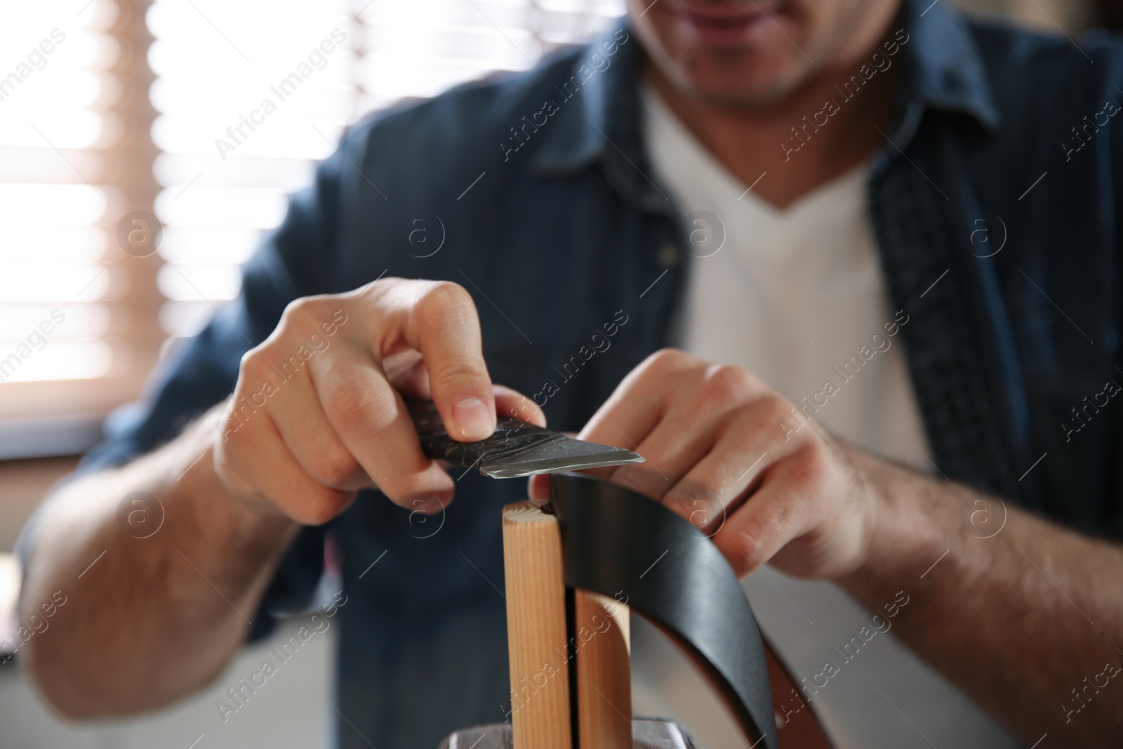 Photo of Man thinning edges of leather belt in workshop, closeup