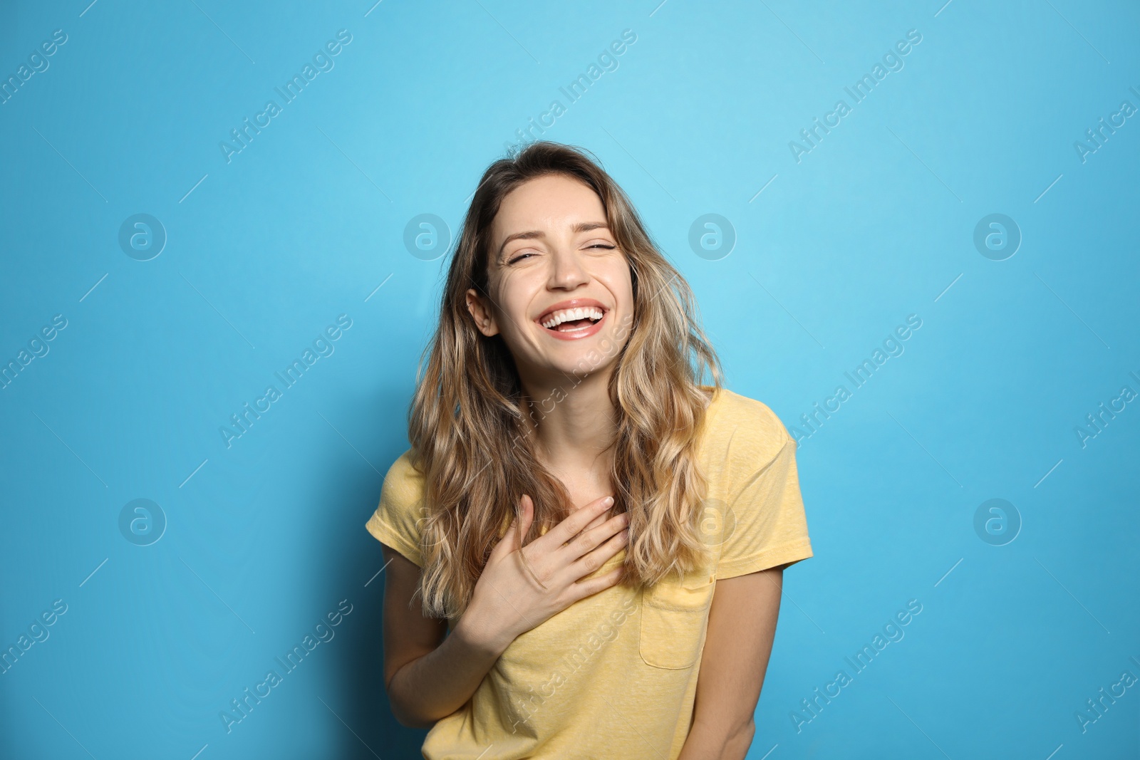 Photo of Cheerful young woman laughing on light blue background