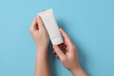 Woman with tube of hand cream on light blue background, top view