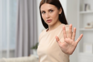 Photo of Woman showing stop gesture at home, selective focus. Space for text