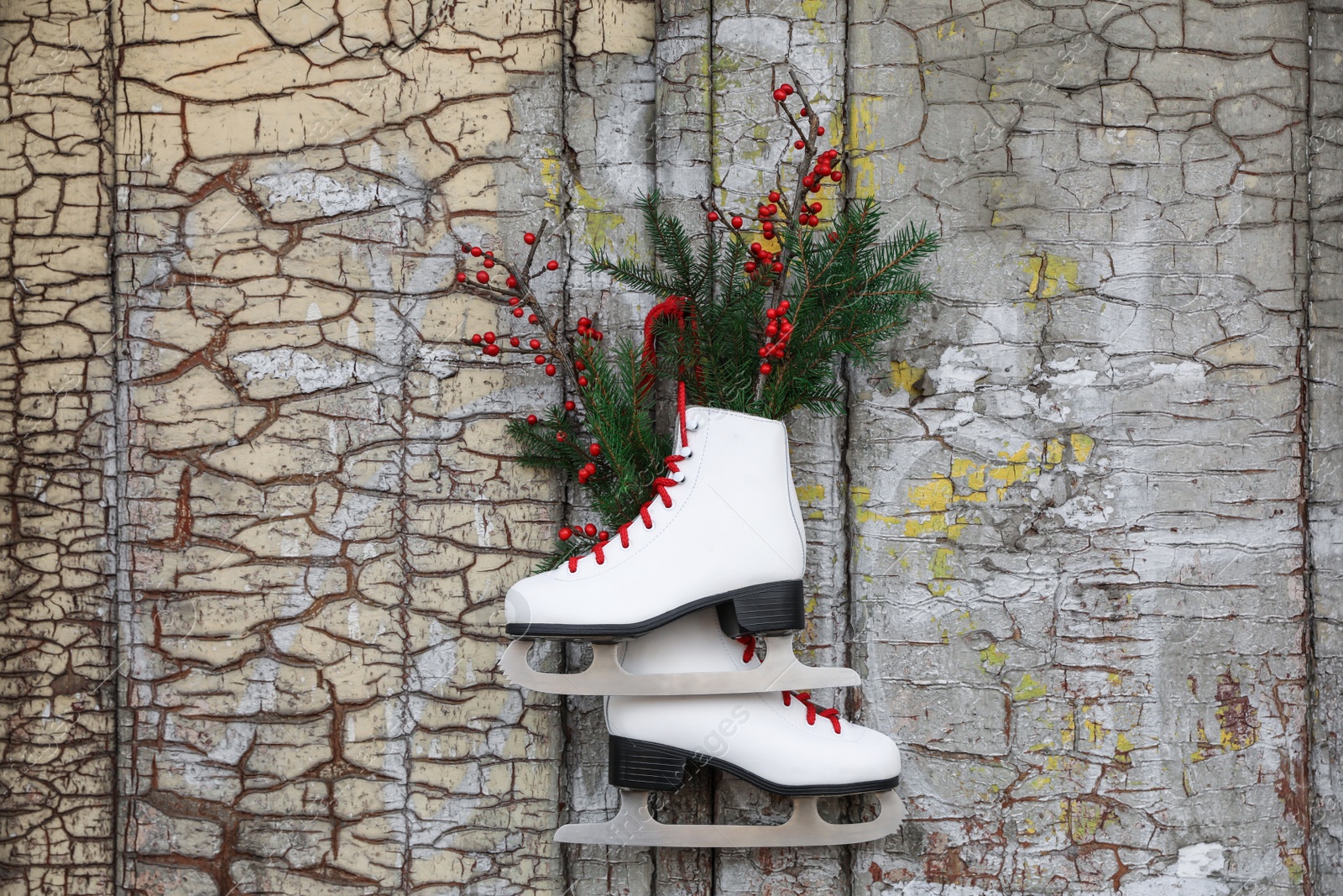 Photo of Pair of ice skates with Christmas decor hanging on old wooden door