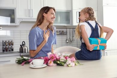 Photo of Little daughter congratulating her mom in kitchen. Happy Mother's Day