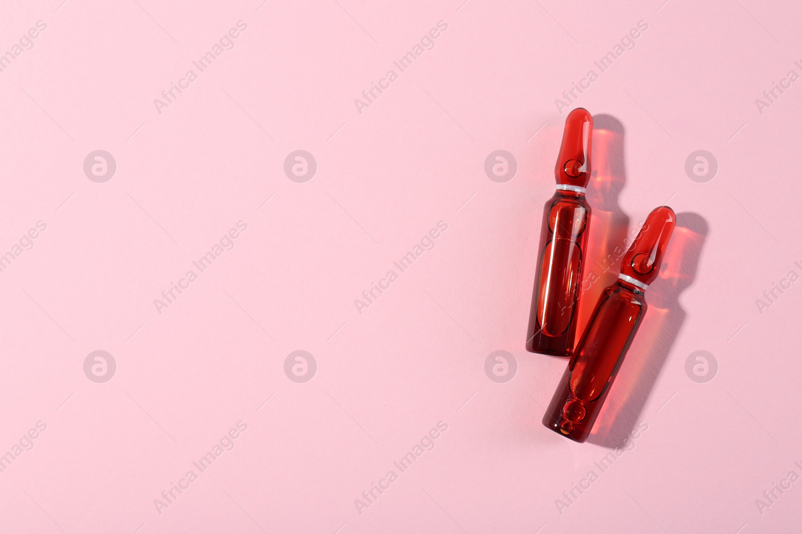 Photo of Glass ampoules with liquid on pink background, top view. Space for text