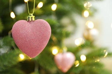 Photo of Beautiful heart shaped holiday bauble hanging on Christmas tree, closeup. Space for text