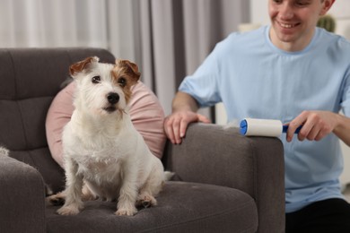 Photo of Smiling man removing pet's hair from armchair at home, closeup