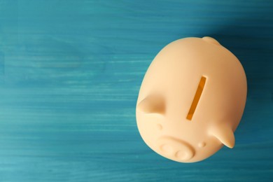 Photo of Ceramic piggy bank on turquoise wooden table, top view. Space for text