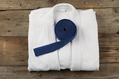 Blue karate belt and white kimono on wooden background, top view