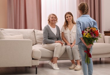 Photo of Little girl congratulating her mom and granny with flowers at home. Happy Mother's Day