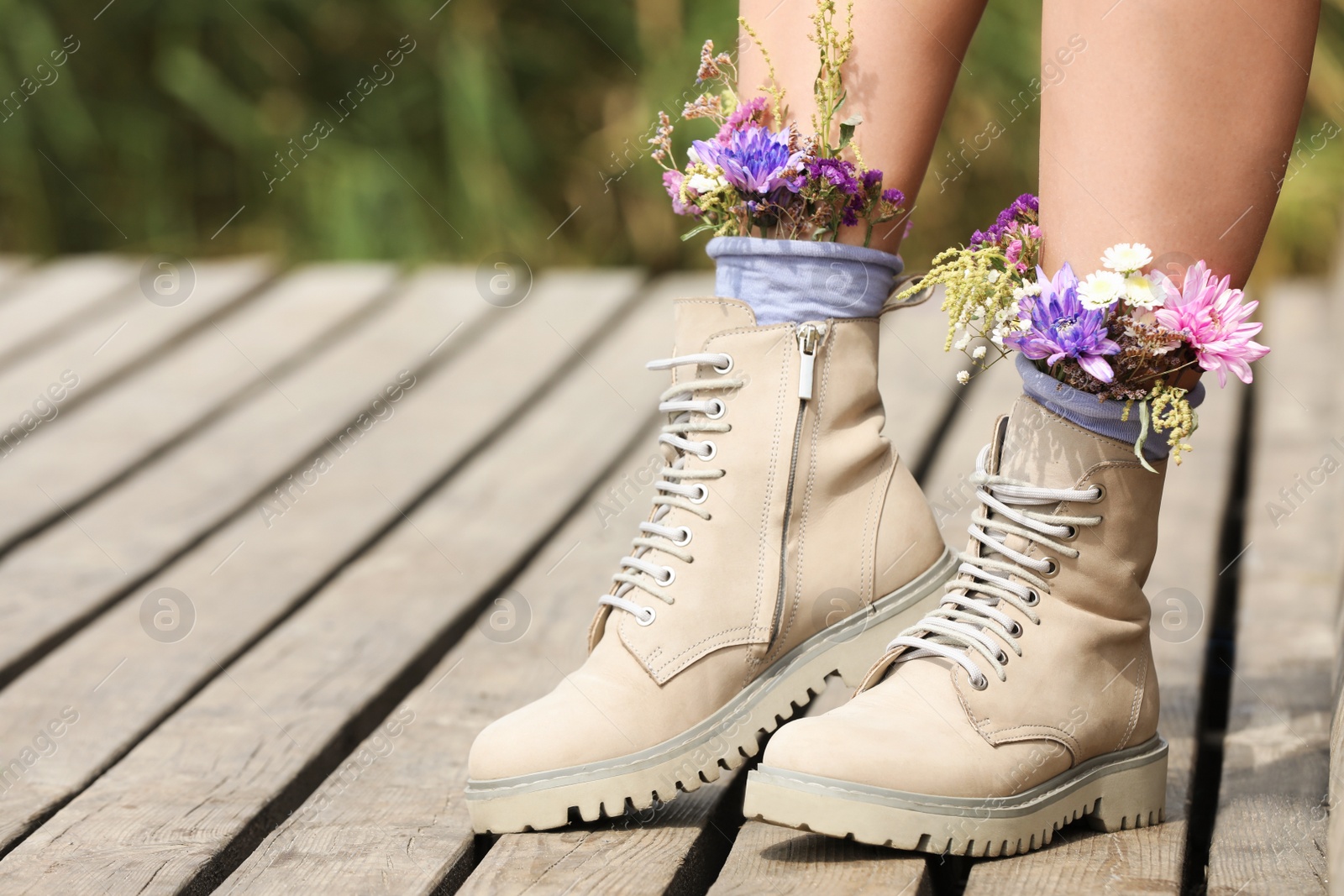 Photo of Woman standing on wooden pier with flowers in socks outdoors, closeup. Space for text