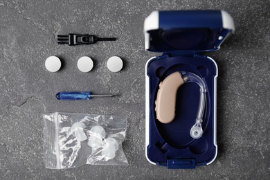 Photo of Flat lay composition with hearing aid and accessories on grey background