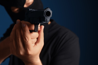Photo of Man in mask holding gun against dark blue background, focus on hands