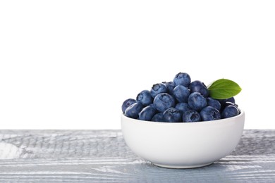 Photo of Tasty fresh blueberries and green leaves in bowl on grey wooden table against white background
