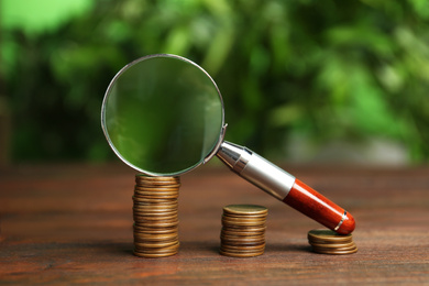 Photo of Coins and magnifying glass on wooden table against blurred background. Search concept