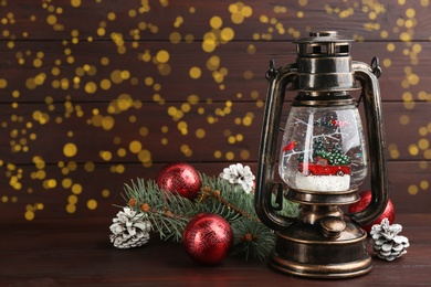 Photo of Beautiful Christmas snow globe in vintage lantern and festive decor on wooden table. Space for text