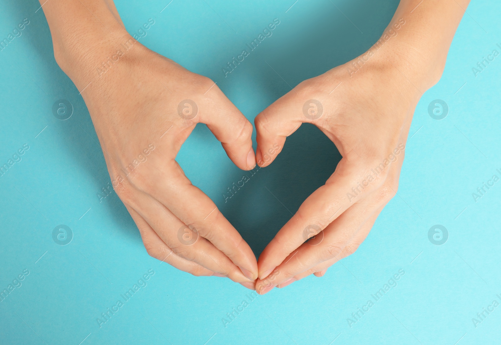 Photo of Woman making heart with her hands on color background, top view