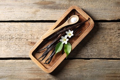 Photo of Vanilla pods, flowers, leaves and spoon with sugar on wooden table, top view