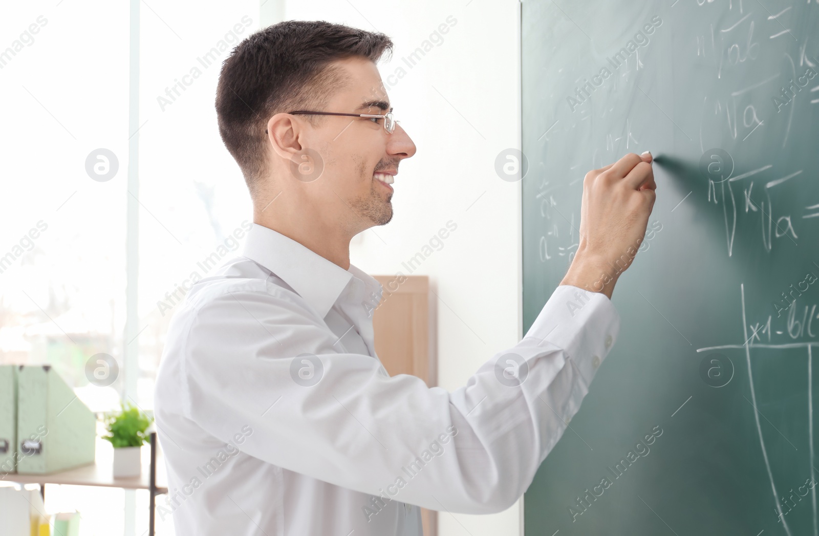 Photo of Young male teacher writing on blackboard in classroom