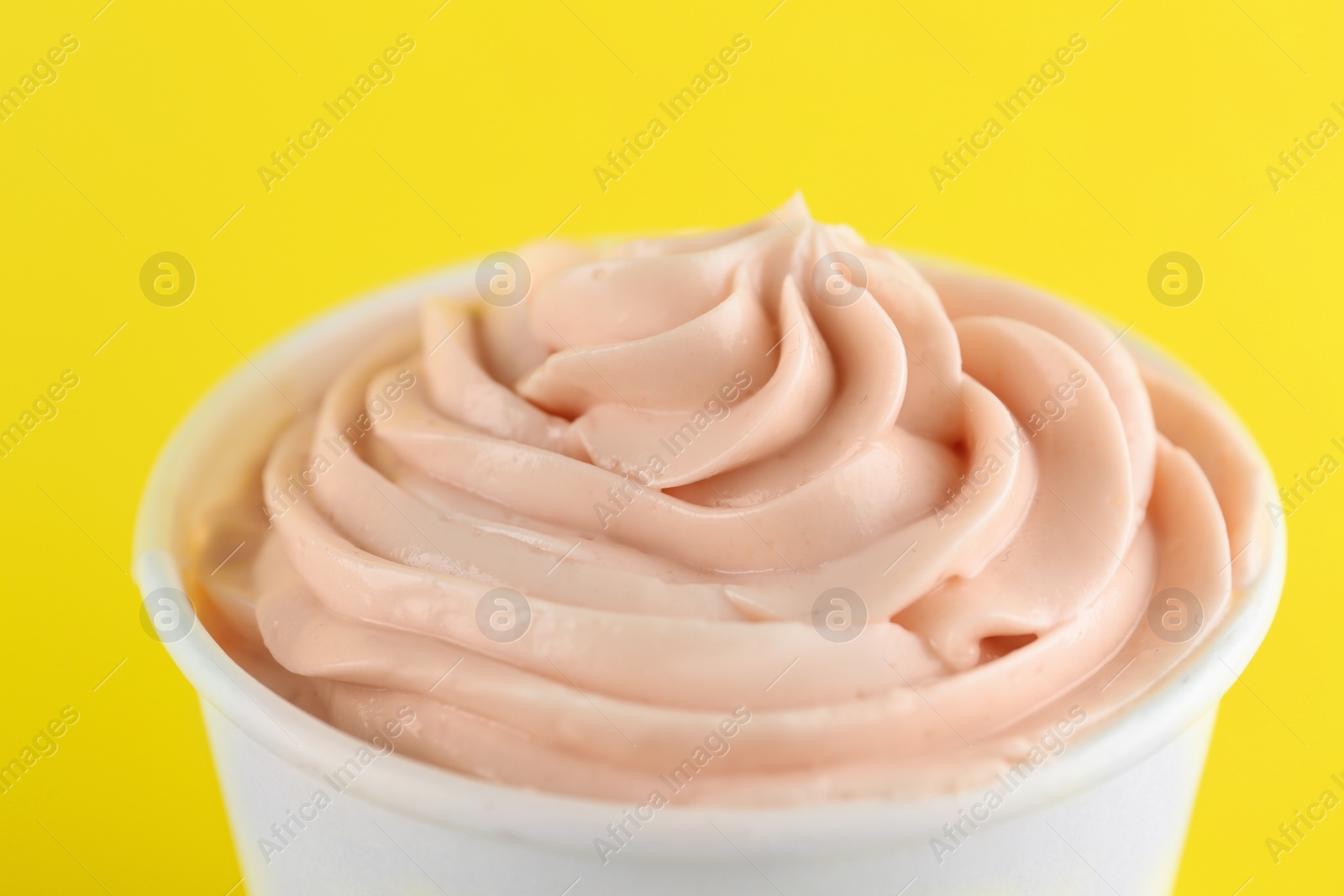 Photo of Cup with tasty frozen yogurt on yellow background, closeup