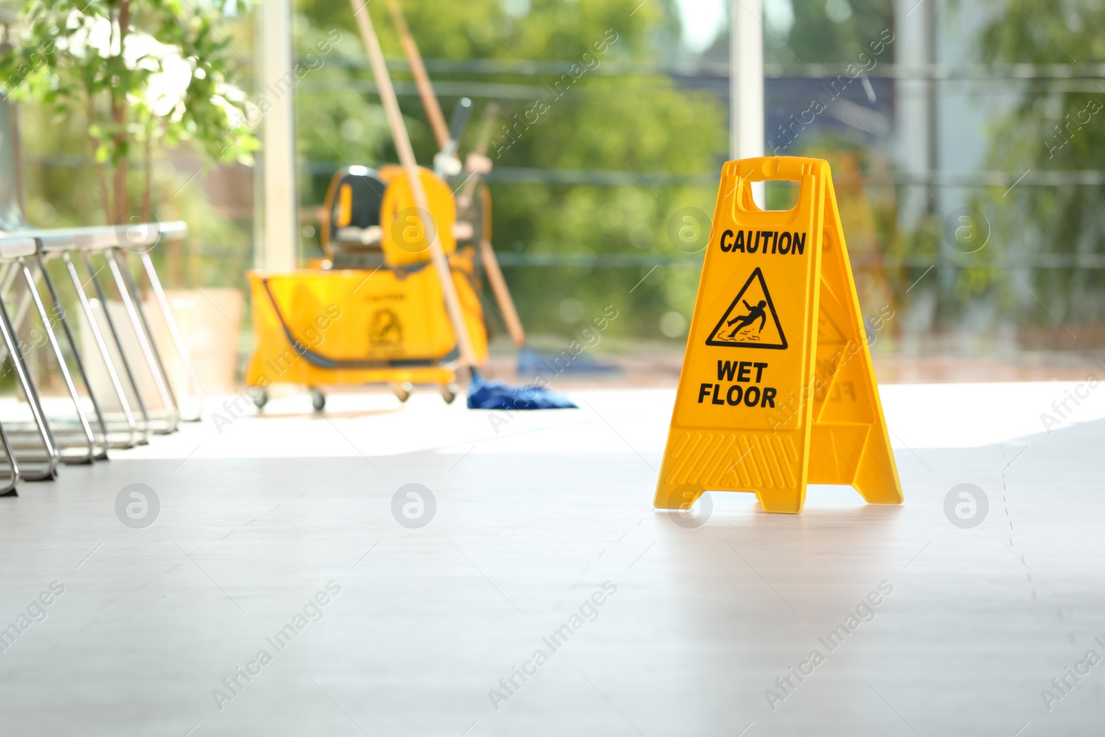 Photo of Safety sign with phrase Caution wet floor and blurred mop bucket on background. Cleaning service