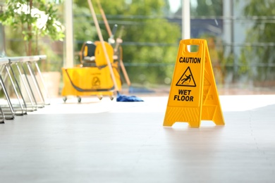 Photo of Safety sign with phrase Caution wet floor and blurred mop bucket on background. Cleaning service