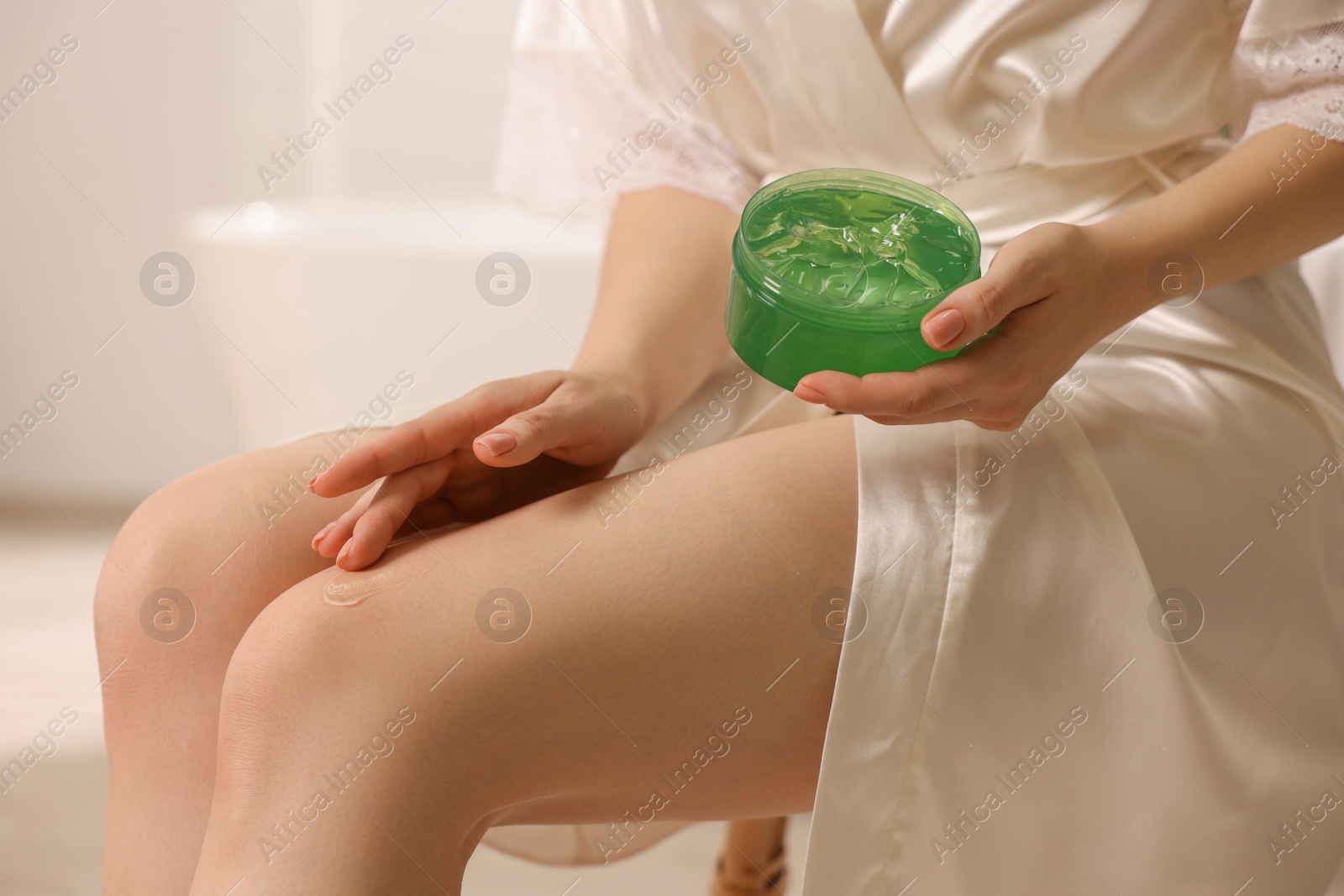 Photo of Young woman applying aloe gel onto leg indoors, closeup