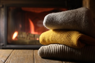 Photo of Stack of sweaters on wooden table near fireplace at home, closeup. Space for text