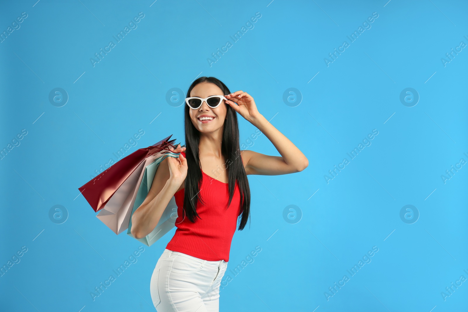 Photo of Beautiful young woman with paper shopping bags on light blue background