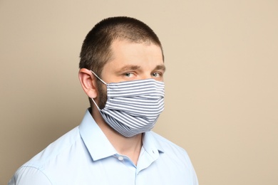 Photo of Man wearing handmade cloth mask on beige background. Personal protective equipment during COVID-19 pandemic