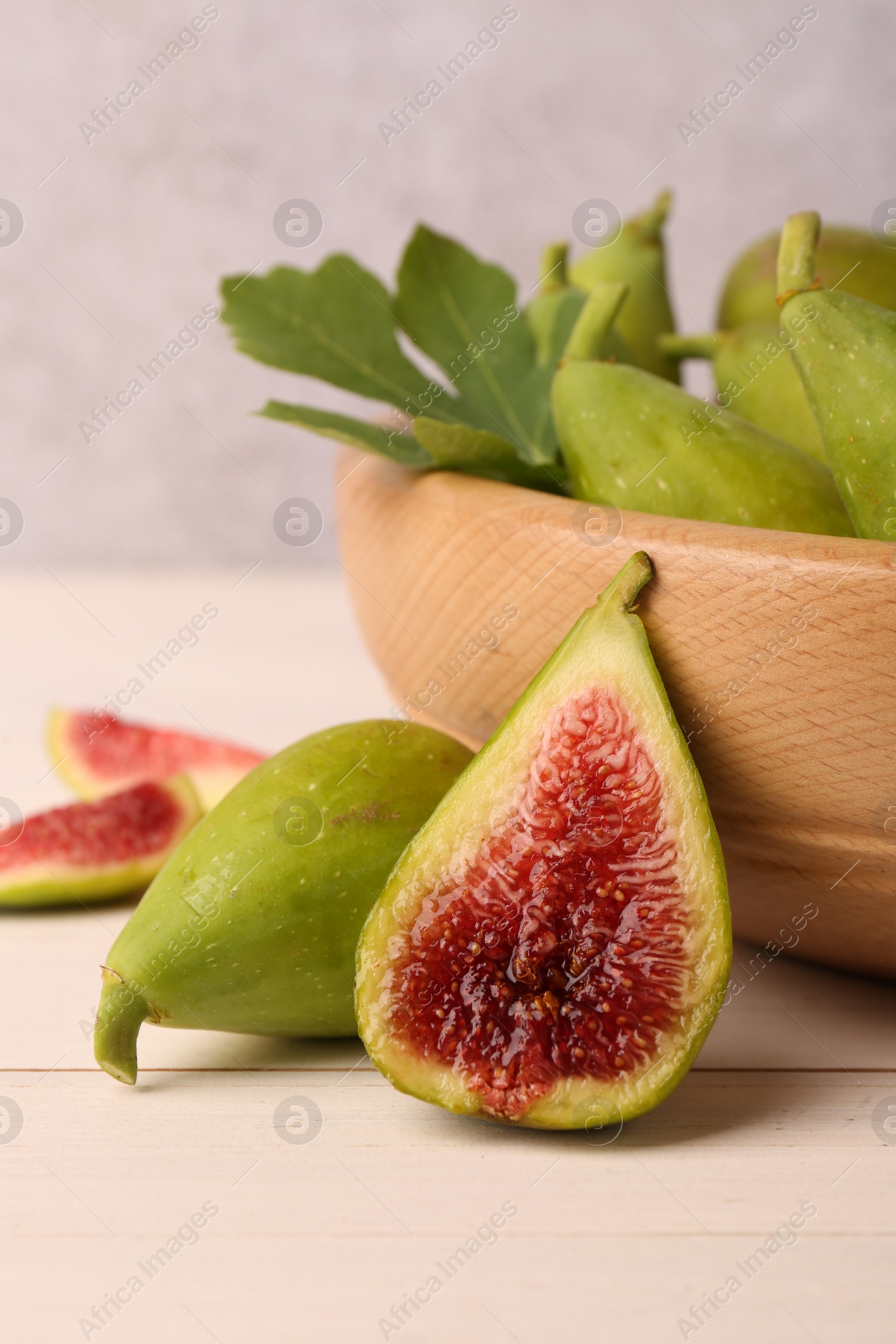Photo of Cut and whole fresh green figs on white wooden table, closeup