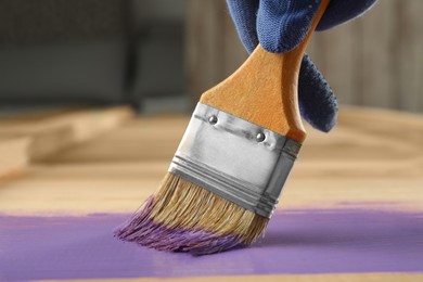 Photo of Worker applying violet paint onto wooden surface, closeup