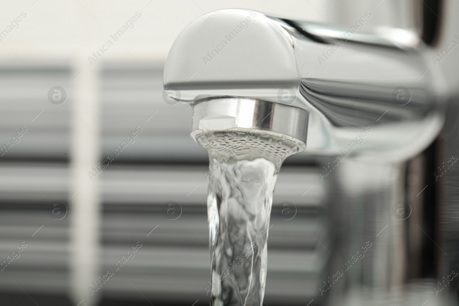 Photo of Water flowing from tap on blurred background, closeup. Space for text