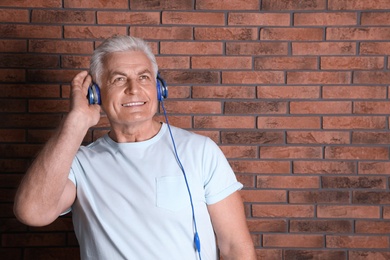Photo of Mature man enjoying music in headphones against brick wall. Space for text