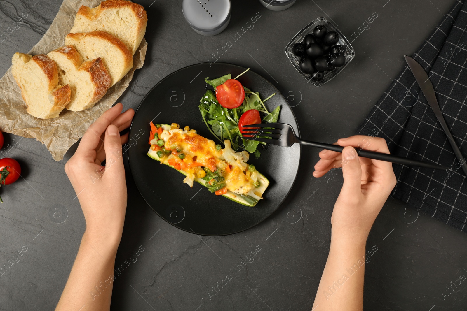 Photo of Woman with baked stuffed zucchini at black table, top view