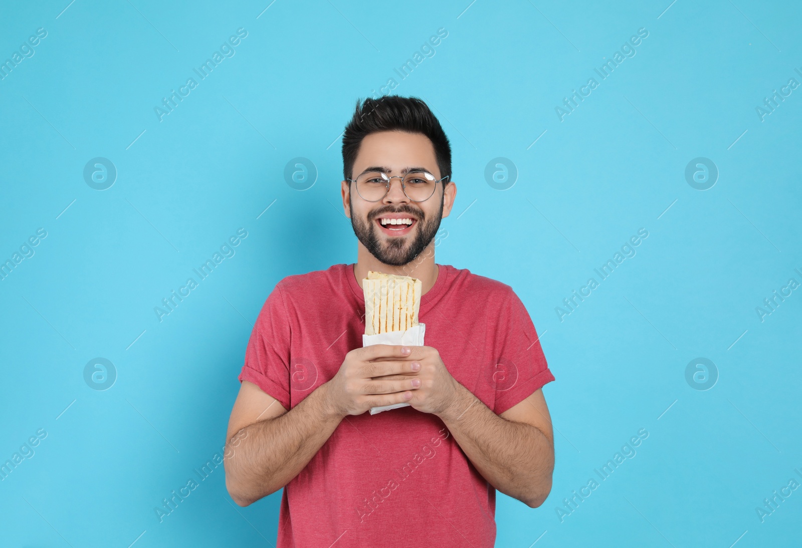 Photo of Happy young man holding tasty shawarma on turquoise background