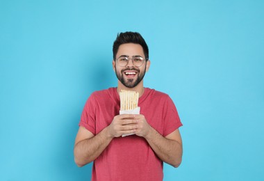 Happy young man holding tasty shawarma on turquoise background