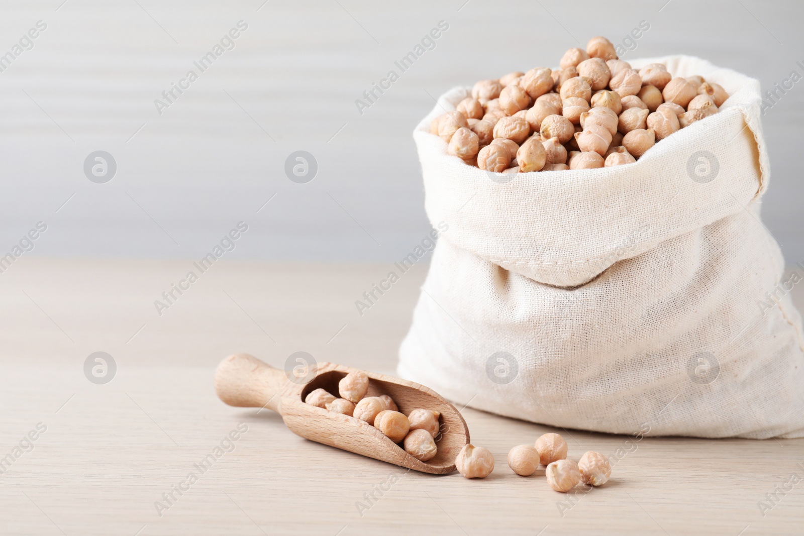 Photo of Sack and scoop with chickpeas on wooden table, space for text