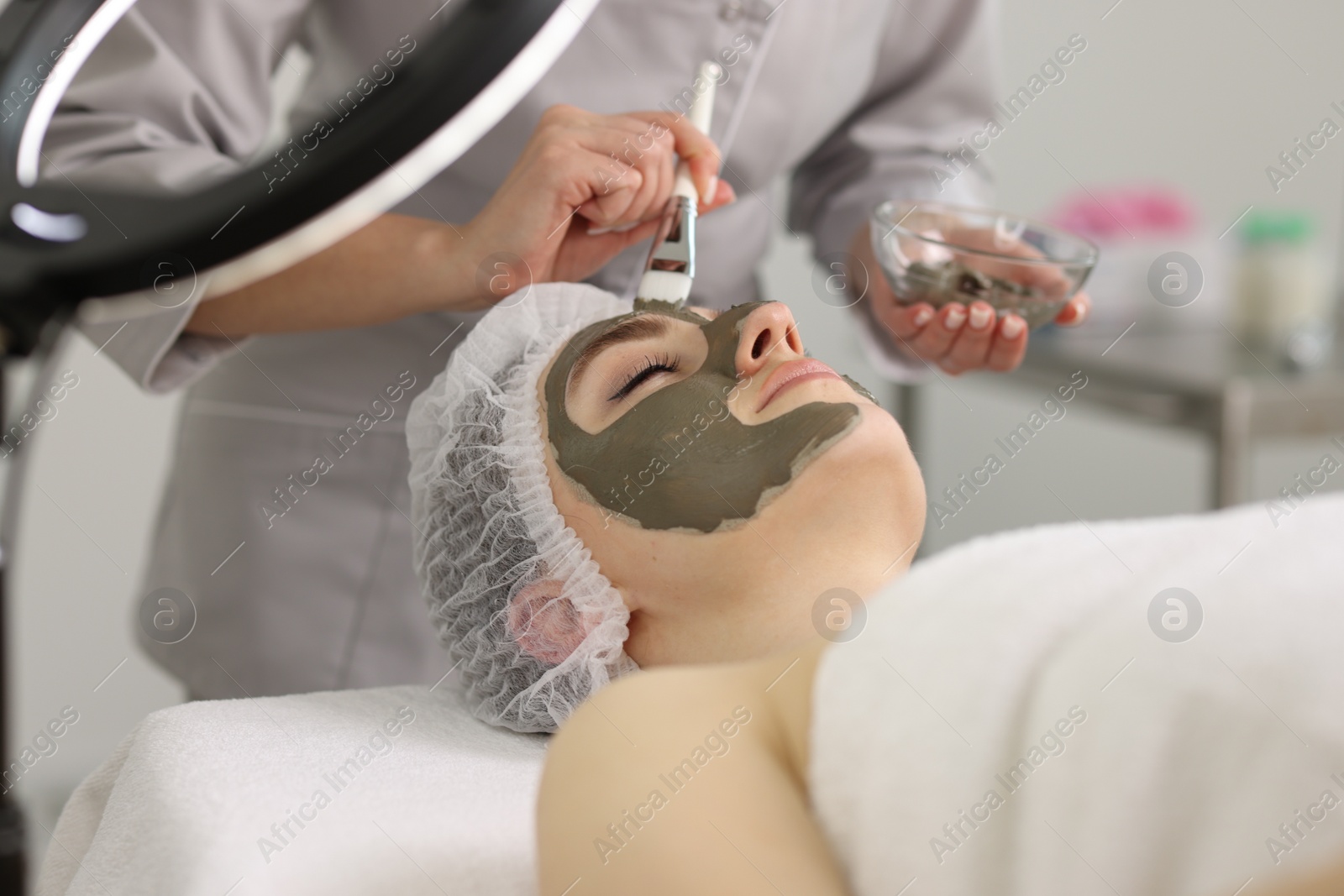 Photo of Cosmetologist applying mask on woman's face in clinic, closeup