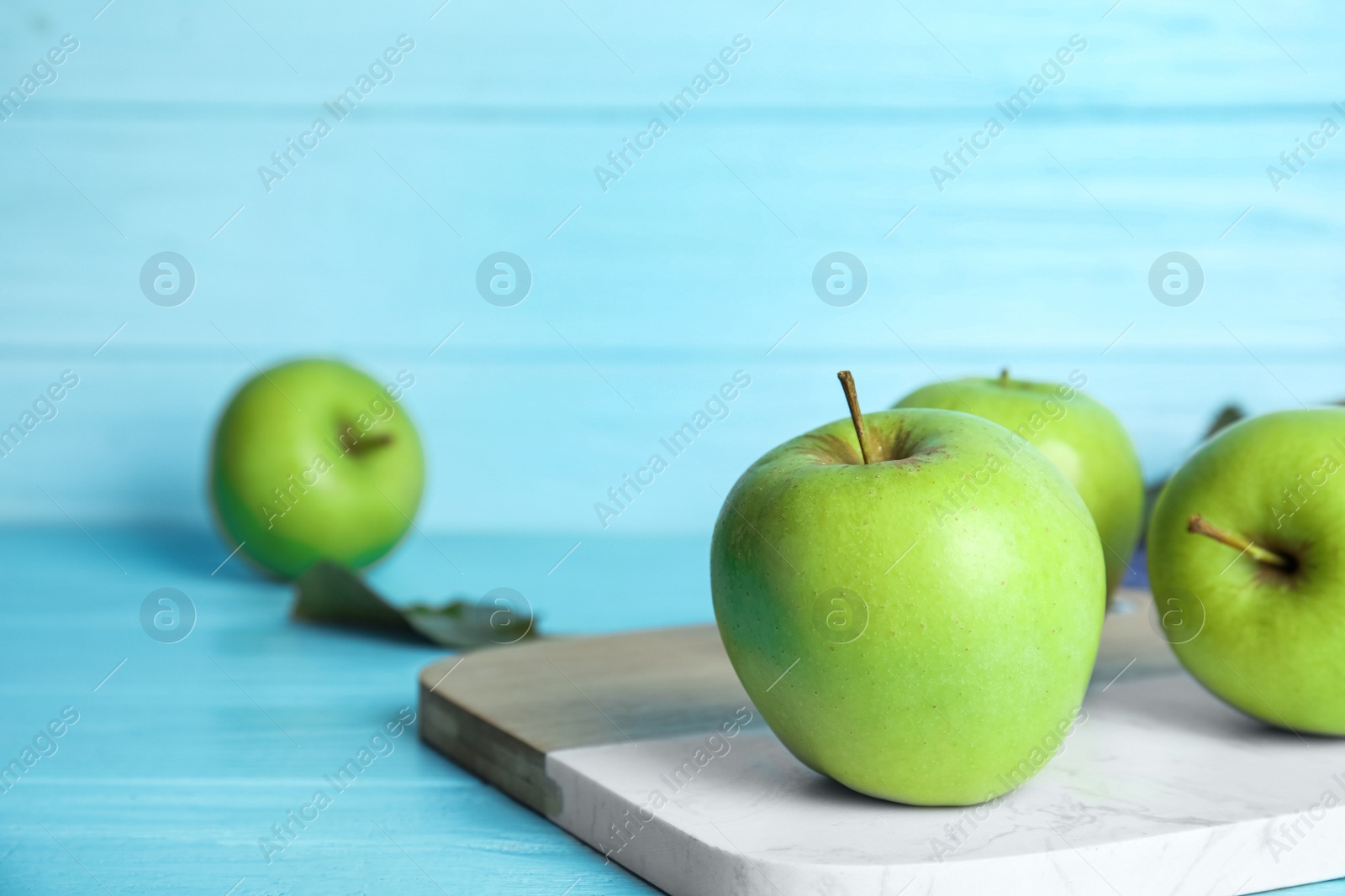 Photo of Ripe green apples on light blue wooden table. Space for text