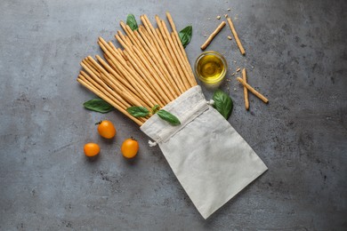 Photo of Delicious grissini sticks, basil leaves, cherry tomatoes and oil on grey table, flat lay