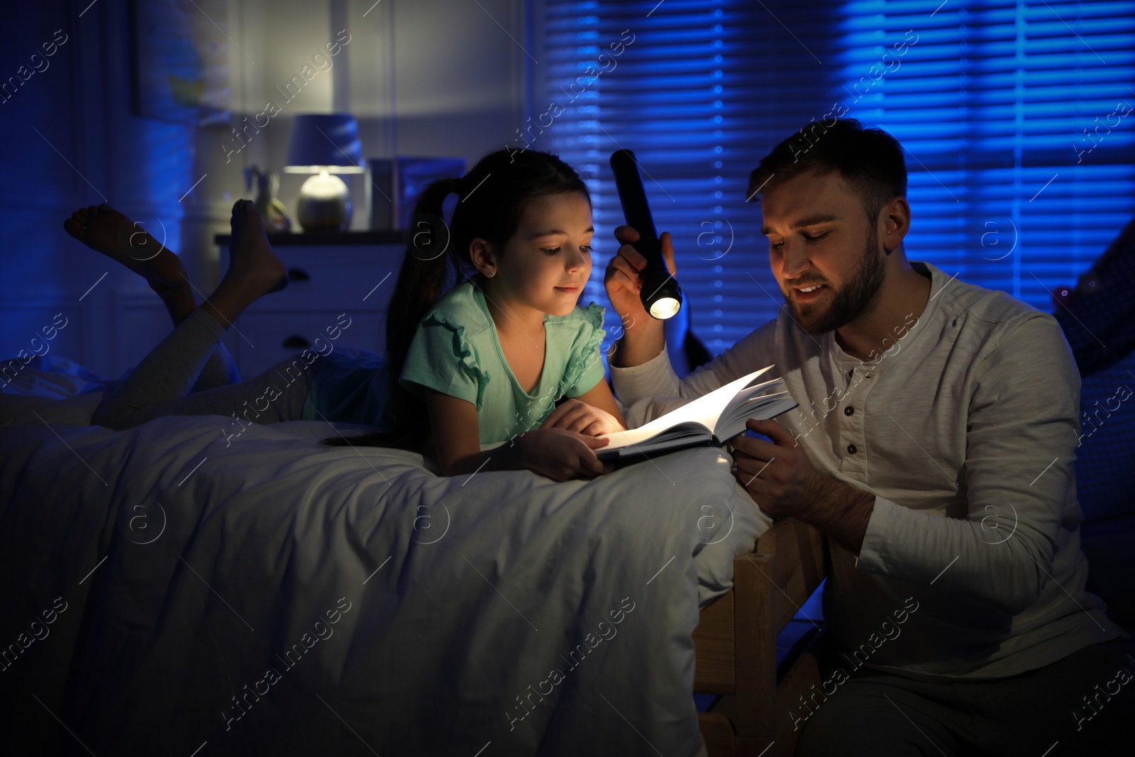 Photo of Father with little daughter reading fairy tale in dark bedroom